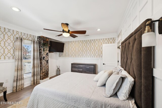 bedroom featuring wood finished floors, a wainscoted wall, crown molding, and wallpapered walls