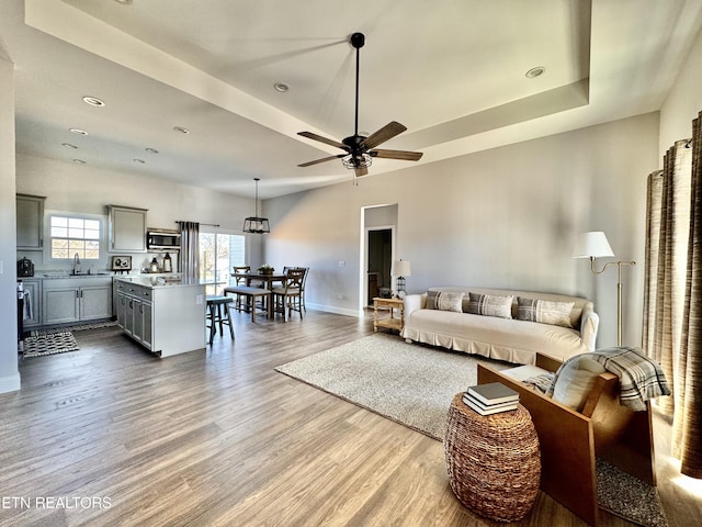 living area with a tray ceiling, baseboards, wood finished floors, and a ceiling fan