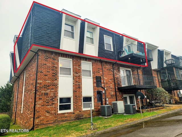 exterior space featuring central air condition unit, mansard roof, and brick siding