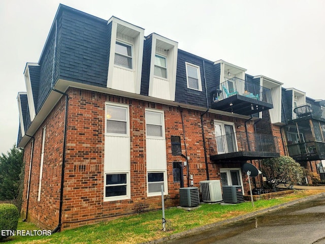 view of home's exterior with a shingled roof, brick siding, central AC, and mansard roof