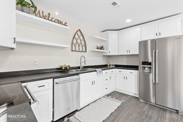 kitchen featuring dark countertops, appliances with stainless steel finishes, wood finished floors, white cabinetry, and open shelves