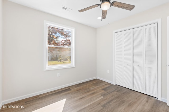 unfurnished bedroom featuring a closet, visible vents, a ceiling fan, wood finished floors, and baseboards