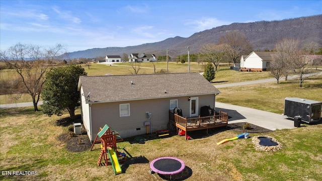 rear view of property featuring a playground, a yard, roof with shingles, a deck with mountain view, and crawl space