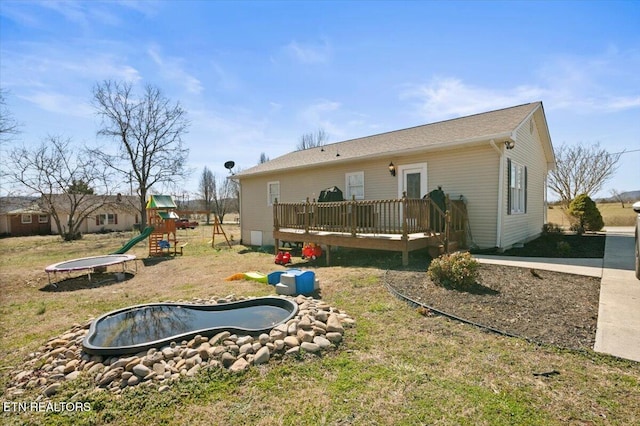 rear view of house featuring a trampoline, a playground, and a wooden deck