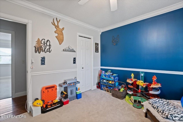 playroom featuring a textured ceiling, ceiling fan, carpet floors, baseboards, and crown molding