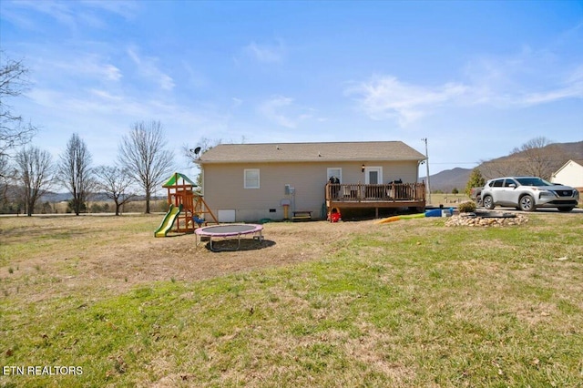 back of house with a lawn, crawl space, a trampoline, a wooden deck, and a playground