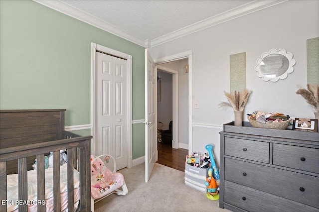 bedroom with a textured ceiling, light colored carpet, baseboards, ornamental molding, and a closet