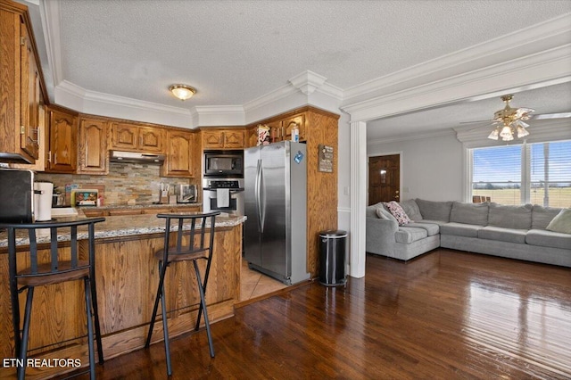 kitchen with appliances with stainless steel finishes, brown cabinetry, a peninsula, wood finished floors, and under cabinet range hood