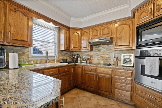 kitchen with black appliances, under cabinet range hood, brown cabinets, and a sink