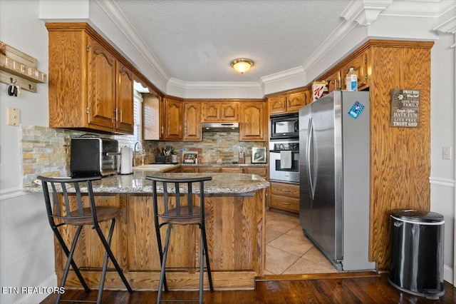 kitchen with brown cabinets, stainless steel appliances, a sink, a peninsula, and under cabinet range hood