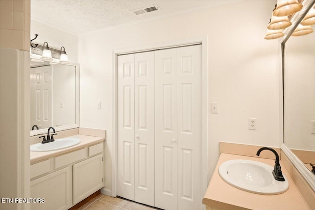 bathroom with a textured ceiling, visible vents, two vanities, and a sink