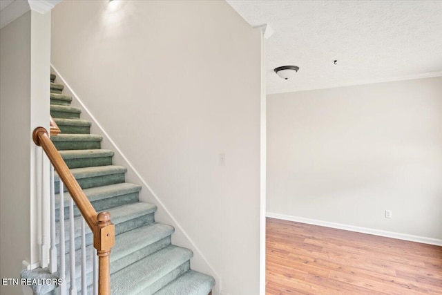 staircase with a textured ceiling, wood finished floors, and baseboards