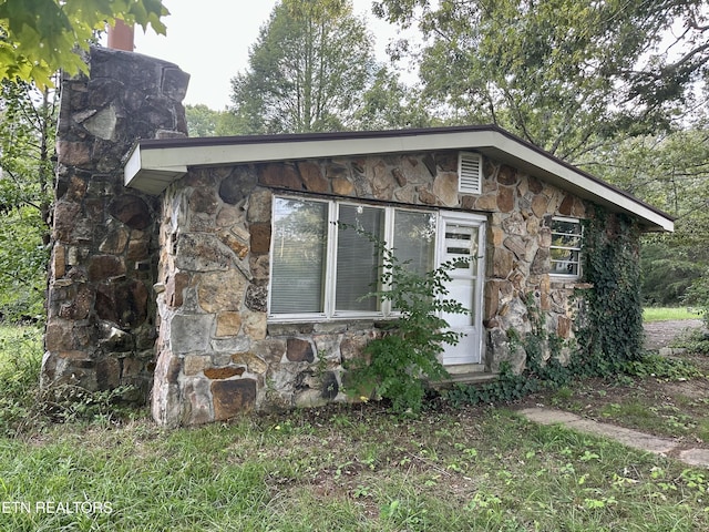 view of side of home with stone siding and a chimney