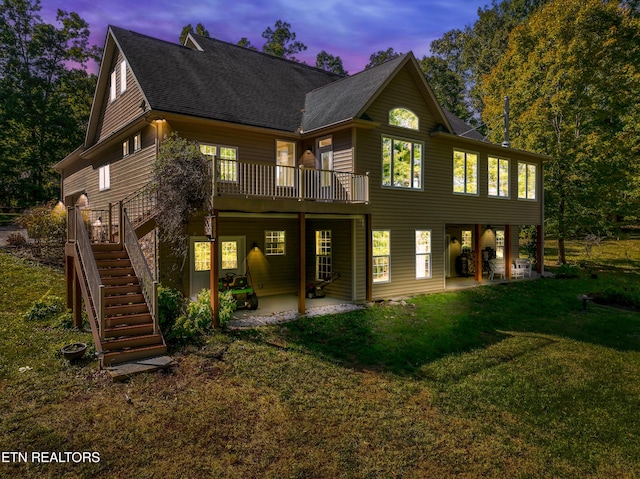 back of house at dusk featuring roof with shingles, a yard, stairs, a deck, and a patio area