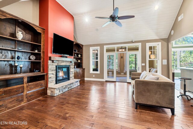 living area featuring wood-type flooring, high vaulted ceiling, a stone fireplace, and built in shelves