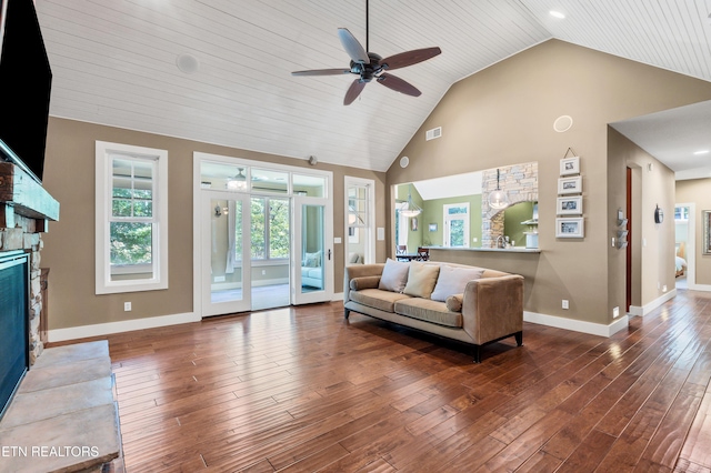 living area with visible vents, high vaulted ceiling, hardwood / wood-style flooring, a stone fireplace, and baseboards