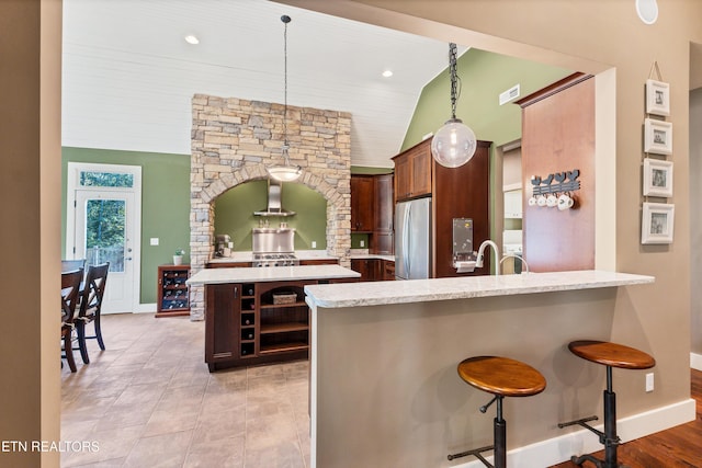 kitchen with a breakfast bar area, a peninsula, open shelves, freestanding refrigerator, and wall chimney exhaust hood