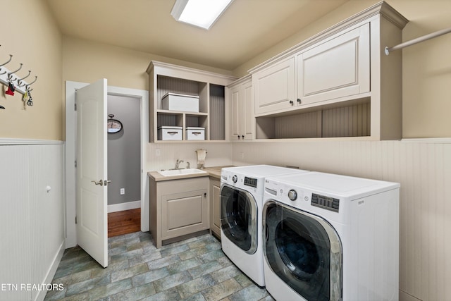 laundry room with washing machine and dryer, stone finish floor, wainscoting, cabinet space, and a sink