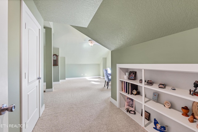 hall with carpet flooring, a textured ceiling, baseboards, and vaulted ceiling