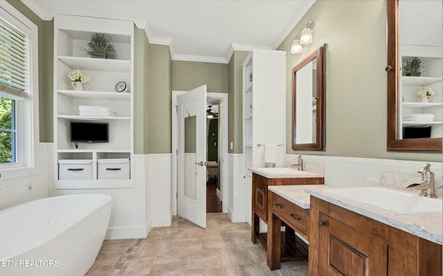 bathroom featuring a wainscoted wall, built in shelves, ornamental molding, a soaking tub, and vanity