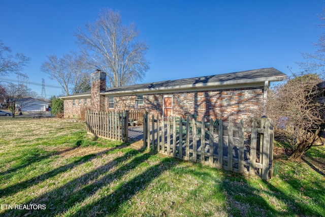 exterior space featuring a yard, fence, brick siding, and a chimney