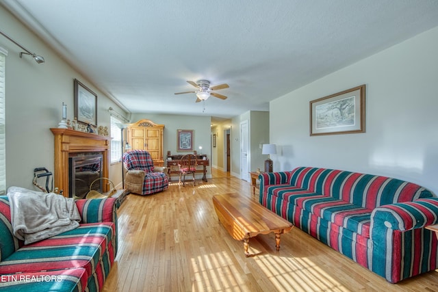 living room featuring a fireplace with raised hearth, a ceiling fan, a textured ceiling, wood-type flooring, and baseboards