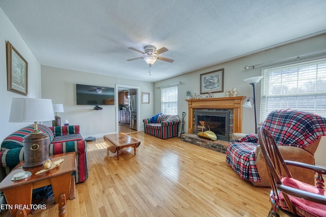 living room featuring a fireplace, hardwood / wood-style floors, a ceiling fan, and a textured ceiling