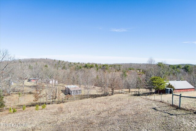 view of yard with an outbuilding, a rural view, fence, and a forest view