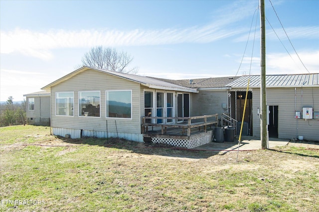 rear view of property featuring metal roof, a deck, and a lawn