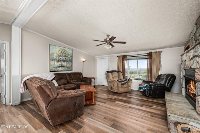 living area featuring crown molding, lofted ceiling, a stone fireplace, a textured ceiling, and wood finished floors