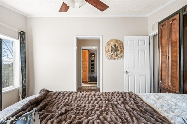 bedroom featuring a textured ceiling, ornamental molding, visible vents, and a ceiling fan