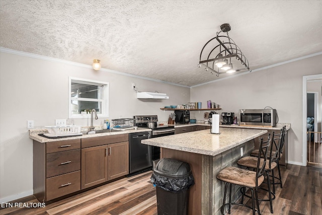 kitchen featuring a sink, light countertops, appliances with stainless steel finishes, ornamental molding, and a kitchen bar