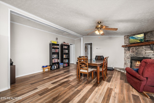 dining room featuring a textured ceiling, ornamental molding, wood finished floors, and a stone fireplace