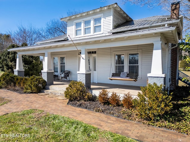 view of front of property featuring brick siding, a chimney, covered porch, a standing seam roof, and metal roof