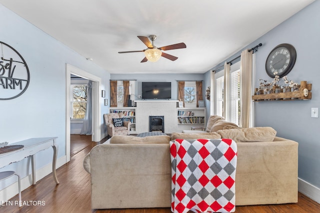 living room featuring a brick fireplace, baseboards, a ceiling fan, and wood finished floors