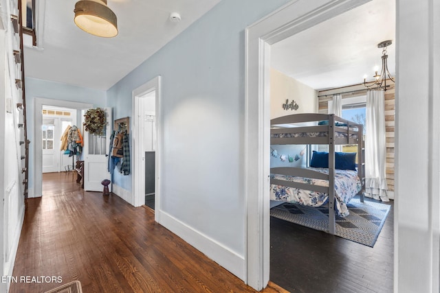 hall with dark wood-style floors, baseboards, and a chandelier