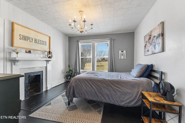 bedroom with a chandelier, a fireplace with raised hearth, and wood finished floors