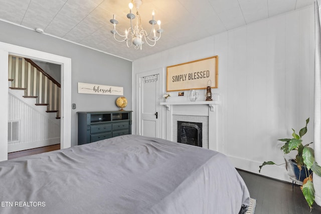 bedroom with baseboards, visible vents, wood finished floors, a fireplace, and a notable chandelier