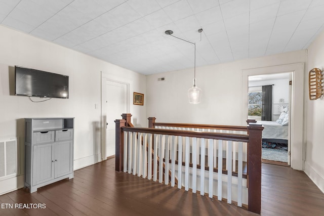 hallway featuring visible vents, dark wood-type flooring, and an upstairs landing