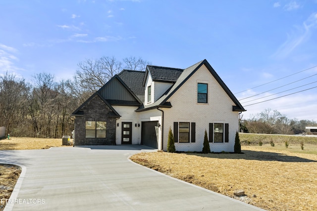 view of front facade with brick siding, a shingled roof, concrete driveway, central AC, and a garage