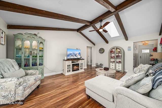 living area with a warm lit fireplace, baseboards, lofted ceiling with skylight, ceiling fan, and wood finished floors