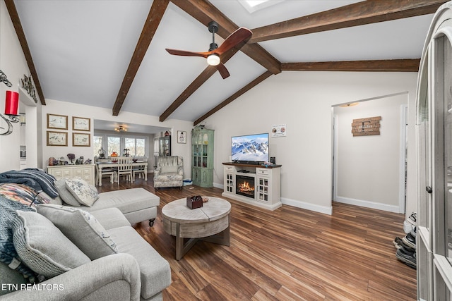 living area featuring baseboards, a ceiling fan, wood finished floors, vaulted ceiling with beams, and a lit fireplace