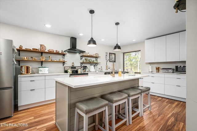 kitchen featuring modern cabinets, appliances with stainless steel finishes, a breakfast bar, wall chimney range hood, and open shelves