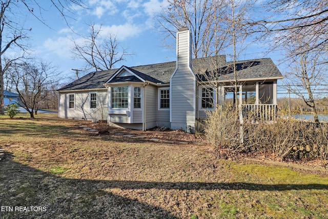 rear view of house featuring roof with shingles, a chimney, and a sunroom