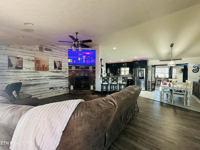 living room featuring a textured ceiling, ceiling fan, a fireplace, and wood finished floors