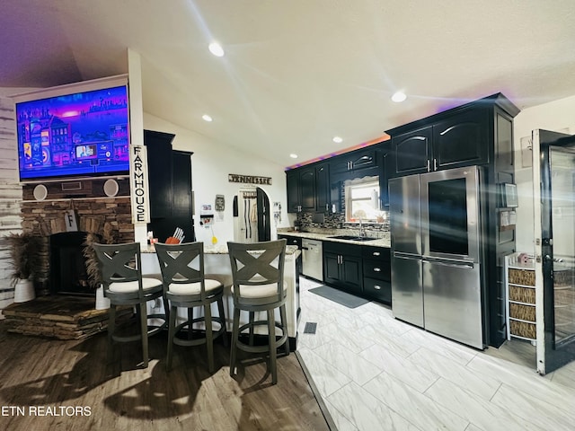 kitchen with stainless steel appliances, lofted ceiling, a sink, a stone fireplace, and a peninsula