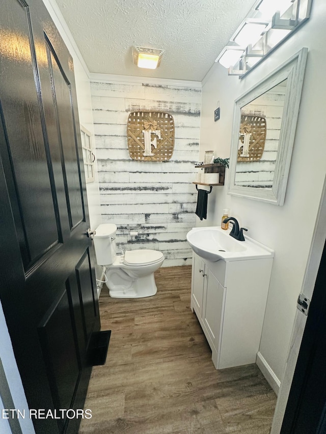 bathroom featuring wooden walls, toilet, wood finished floors, a textured ceiling, and vanity