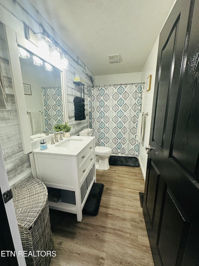 bathroom featuring a shower with shower curtain, toilet, vanity, a textured ceiling, and wood finished floors