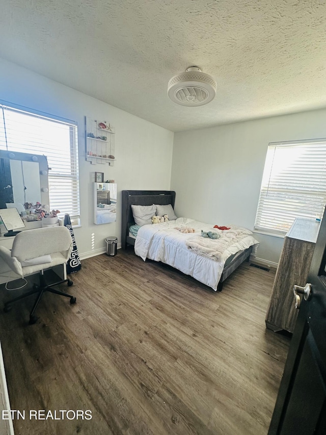 bedroom with visible vents, a textured ceiling, baseboards, and wood finished floors