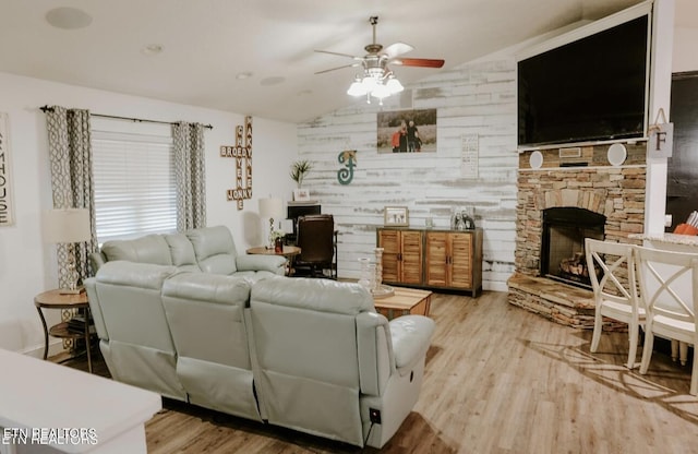 living room featuring vaulted ceiling, ceiling fan, a stone fireplace, and wood finished floors